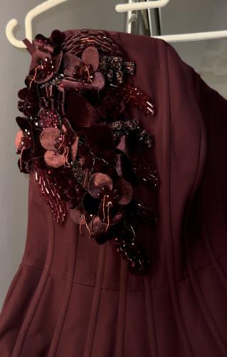 An elegant dress made of burgundy crepe fabric, adorned and embellished with roses, crystals, and prominent beads.