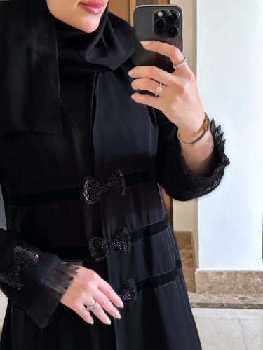 عباية فاخرة بتفاصيل أنيقة تجمع بين الكريب والمخمل والتل المخملي المنقط، مزينة بربطة يدويّة بالشُك الأسود