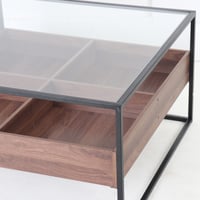 طاولة قهوة وسط بسطح زجاجي وقواعد معدن