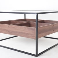 طاولة قهوة وسط بسطح زجاجي وقواعد معدن