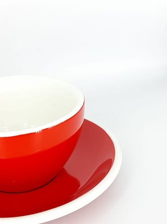 كوب سيراميك أحمر مع صحن على خلفية بيضاء