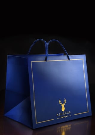 كيس هدايا ازرق وذهبي عليه شعار غزال على خلفية سوداء