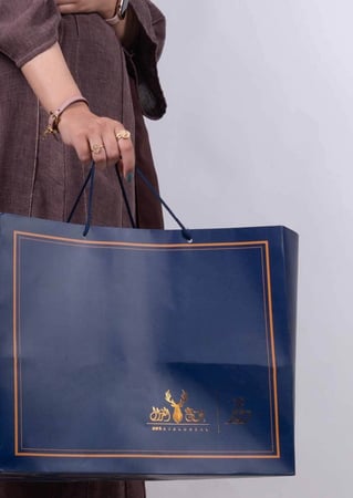 كيس هدايا ازرق من متجر عاج الغزال في يد بنت تلبس عباية و خواتم واساور