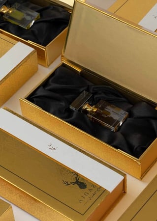 علب توزيعات دهن العود بلون ذهبي عليها اسماء من متجر عاج الغزال