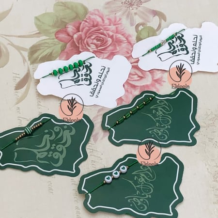 توزيعات اساور  مع ثيم ورقي عن اليوم الوطني نحلم ونحقق  ( 12 قطعه )