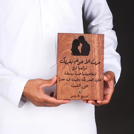 شخص يحمل هدية خشب الماهوجني المحفورة بالليزر توضح حجم المنتج ودقة التف