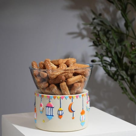 وعاء زجاجي شفاف دائري يحتوي على موالح موضوع فوق قاعدة سيراميك بيضاء مر