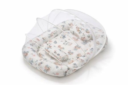 رضيع نائم في عش نوم مبطن مع وسائد جانبية وناموسية