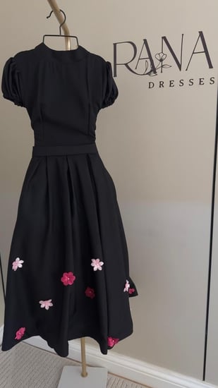 فستان أسود أنيق مزين بورود ملونة بتدرجات الوردي فوشي على الجوانب، بقصة ناعمة وأكمام قصيرة.