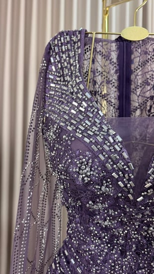 فستان سهرة بنفسجي، مطرز ببريق ناعم يعكس الفخامة،أكمام شفافة تمنحك حضورًا أنيقًا ولمسة من السحر والجاذبية.