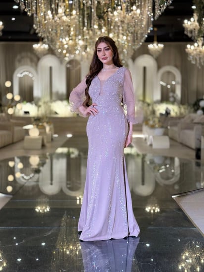 فستان سهرة لحمي ناعم، بقصّة ضيقة تبرز القوام وياقة على شكل V، مع أكمام شفافة.مزين بتطريز لامع يمنحه بريقًا أنيقًا.