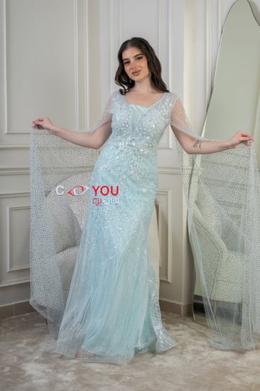 فستان سهرة سماوي مطرّز بقصّة عمودية ورقبة مربعة مع كاب شفاف مرصّع.