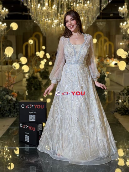 فستان أوف وايت مطرّز بخيوط فضية بقصّة رقبة V مبطّنة وأكمام شفافة منفوشة وتنورة واسعة أنيقة. مثالي للأفراح والسهرات.