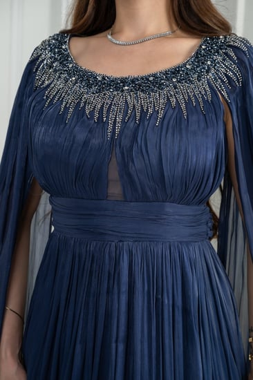 فستان سهرة كحلي يوقّع حضورك بأسلوب ملكي. قماش حريري مطوي ينساب بانعكاس لامع مع كل حركة.