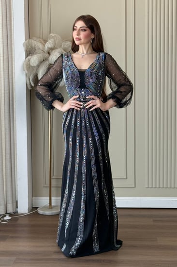 فستان سهرة اسود ناعم، بقصّة ضيقة تبرز القوام وياقة على شكل V، مع أكمام شفافة.مزين بتطريز لامع يمنحه بريقًا أنيقًا.