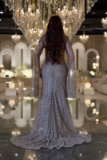 فستان سهرة تستحقّين فستانًا يلمع بقدرك هذا السيلفر المطرّز بالكامل برقبة عالية وأكمام كاب متدفّقة صُمّم ليبرز جمالك برقيّ