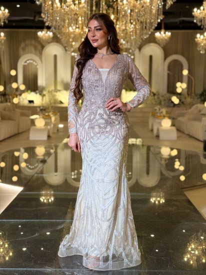 فستان سهرة أوف وايت مطرّز كريستالات بأكمام شفافة وقصّة عمودية