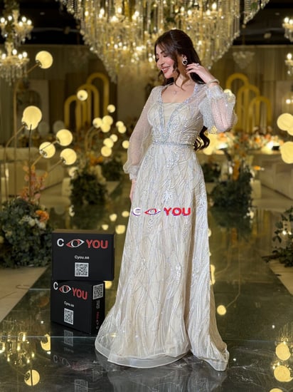 فستان أوف وايت مطرّز بخيوط فضية بقصّة رقبة V مبطّنة وأكمام شفافة منفوشة وتنورة واسعة أنيقة. مثالي للأفراح والسهرات.