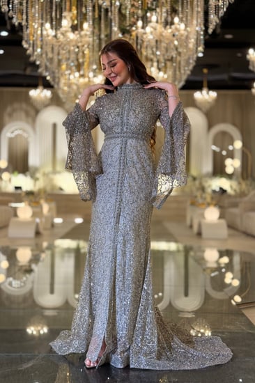 فستان سهرة تستحقّين فستانًا يلمع بقدرك هذا السيلفر المطرّز بالكامل برقبة عالية وأكمام كاب متدفّقة صُمّم ليبرز جمالك برقيّ