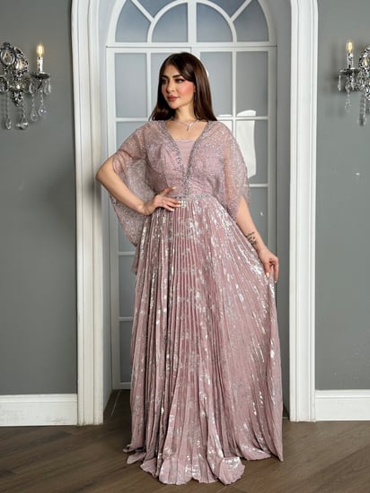 تألقي بفستان سهرة وردي بليسيه لامع وأكمام كاب؛ تصميم فاخر يضيف بريقاً ناعماً لإطلالة لا تُنسى في حفلات الزفاف والمناسبات الخاصة.