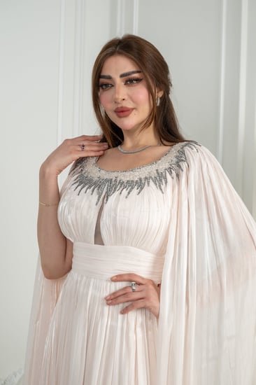 فستان سهرة أوف وايت يفيض نعومة ملكية. قماش حريري مطوي يلتقط الضوء بانعكاس ناعم مع كل حركة.