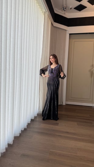 فستان سهرة اسود ناعم، بقصّة ضيقة تبرز القوام وياقة على شكل V، مع أكمام شفافة.مزين بتطريز لامع يمنحه بريقًا أنيقًا.