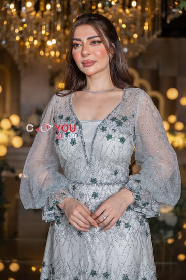 فستان سهرة أبيض مطرز بزهور خضراء أنيقة مع أكمام شفافة منفوشة بتصميم فاخر، لإطلالة ملكية في حفلات الزواج والمناسبات المميزة.