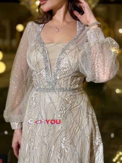 فستان أوف وايت مطرّز بخيوط فضية بقصّة رقبة V مبطّنة وأكمام شفافة منفوشة وتنورة واسعة أنيقة. مثالي للأفراح والسهرات.