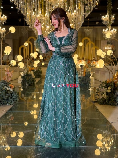 فستان سهرة أخضر داكن مطرّز بخطوط لامعة بقصّة وحزام خرزي وأكمام شفافة