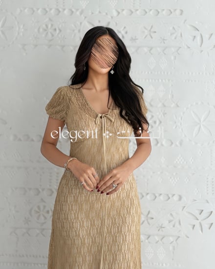 فستان دانتيل بلون ذهبي راق بقصة أنثوية وأكمام قصيرة وتفصيل ربطة أمام