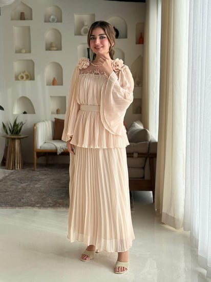 فستان مزوّد بتفاصيل ورود ناعمة على الصدر، وأكمام واسعة مع كسرات