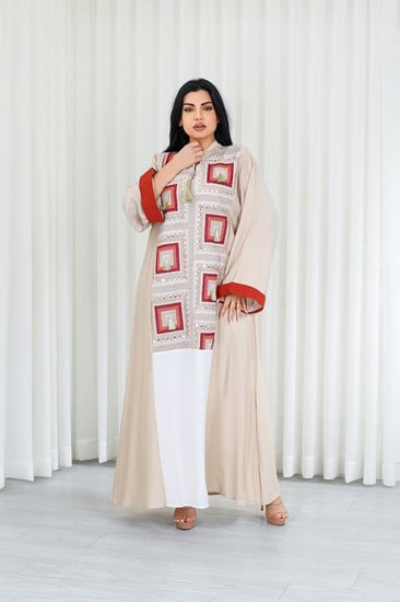 جلابية قماش بطول يصل للكاحل وياقة صغيرة مفتوحة على الصدر مزينة بتطريزات بشكل مربعات على القماش الأمامي وبلون أبيض سادة بأسفل القماش ونهايات أكمام محددة