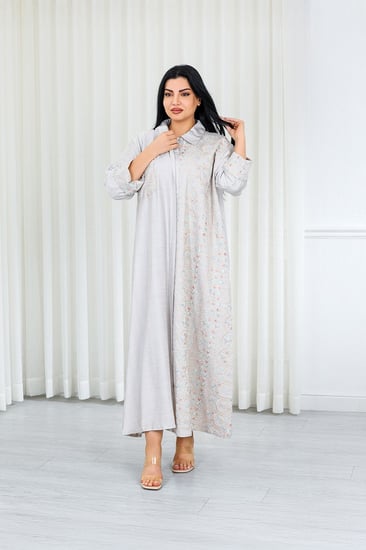 جلابية قماش بطول يصل للكاحل بأزرار مخفية وياقة بأكمام مطوية مزينة بتطريزات بنهاية الأكمام وعلى جانب الجلابية مزودة بجيبة على الصدر