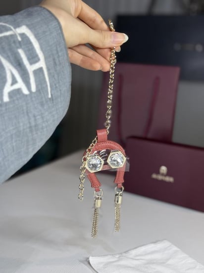 تعليقة اجنر باللون الوردي المرصع بالاحجار على شكل حذوه من الجلد الوردي Aigner pink charm with stones and tassels