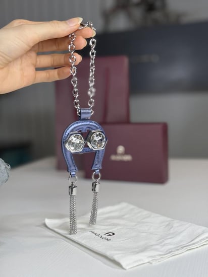 تعليقة اجنر باللون الازرق المعدني اللامع على شكل حذوه من الجلد الوردي Aigner metallic blue charm with stones and tassel's