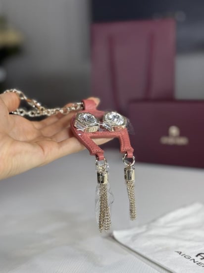 تعليقة اجنر باللون الوردي المرصع بالاحجار على شكل حذوه من الجلد الوردي Aigner pink charm with stones and tassels