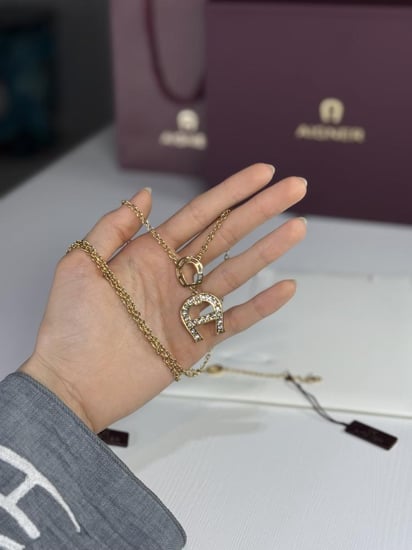 طقم اجنر سلسلة و اسوار ذهبي بالعلامه المرصع بالكريستال A670128. B20 Aigner gold necklace and bracelet set women