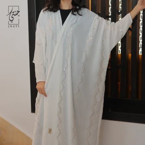 A white half-bisht abaya decorated with elegant go...