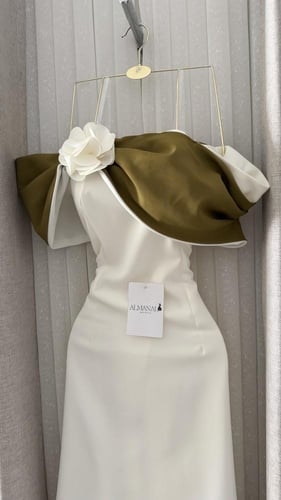 فستان أبيض ناعم بوشاح زيتوني وزهرة بارزة.