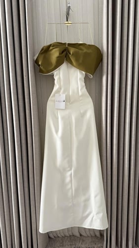 فستان أبيض ناعم بوشاح زيتوني وزهرة بارزة.