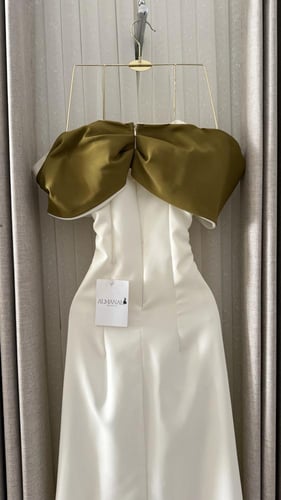 فستان أبيض ناعم بوشاح زيتوني وزهرة بارزة.