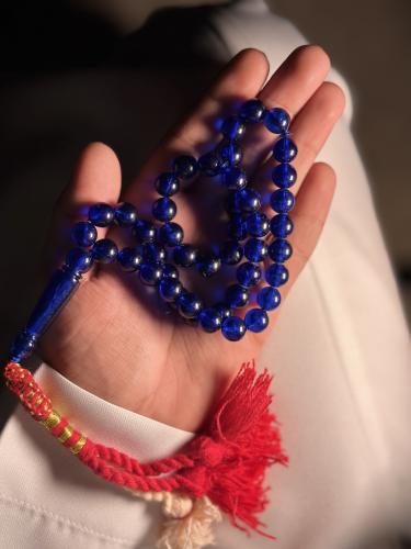 A prayer bead with a blue color and a red tassel