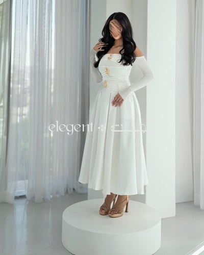 فستان أبيض أنيق بكتف ساقط وتفاصيل ذهبية