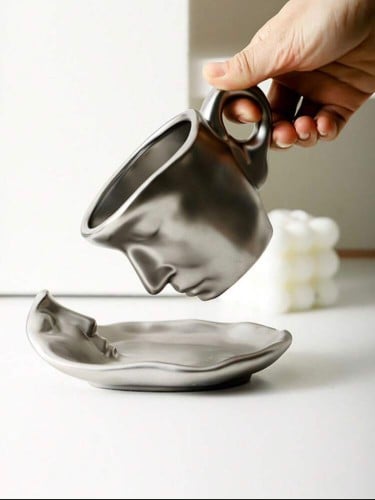 كوب قهوة فضي مع طبق بتصميم وجه
