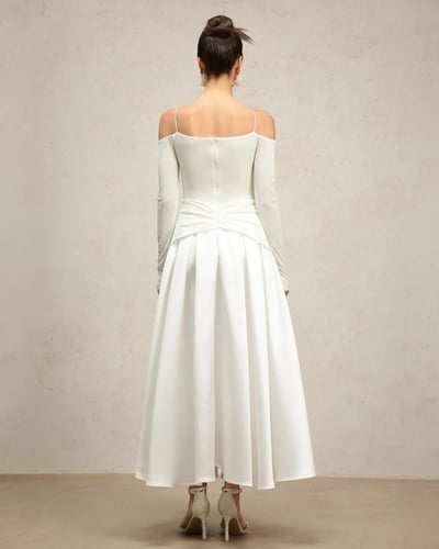 فستان أبيض كريمي بأكتاف مكشوفة وأكمام طويلة