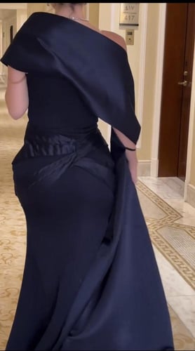 فستان أسود راقٍ بقصّة كتف واحد، مزوّد بوشاح جانبي...