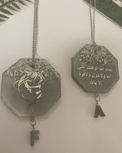 تعليقة سيارة وجهي بلون فضي مزينه بحرف صغير من الري...