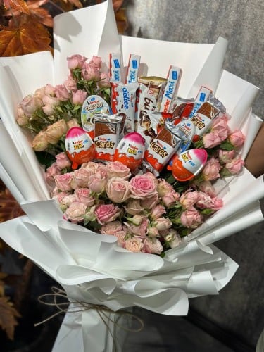 تشكيلة منوّعة من حلويات كندر منسقة وسط بوكيه ورد ط...