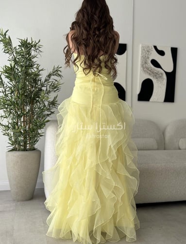 فستان سهرة أصفر مزيّن بطبقات ناعمة وفتحة أمامية