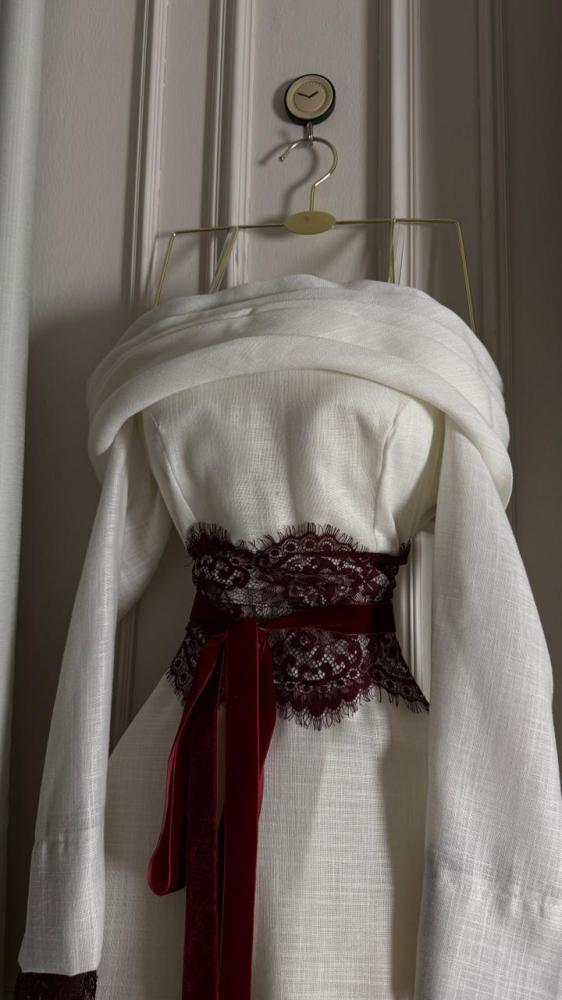 فستان طويل من الكتان الأبيض بياقة "درابيه" وحزام دانتيل عنابي فاخر.